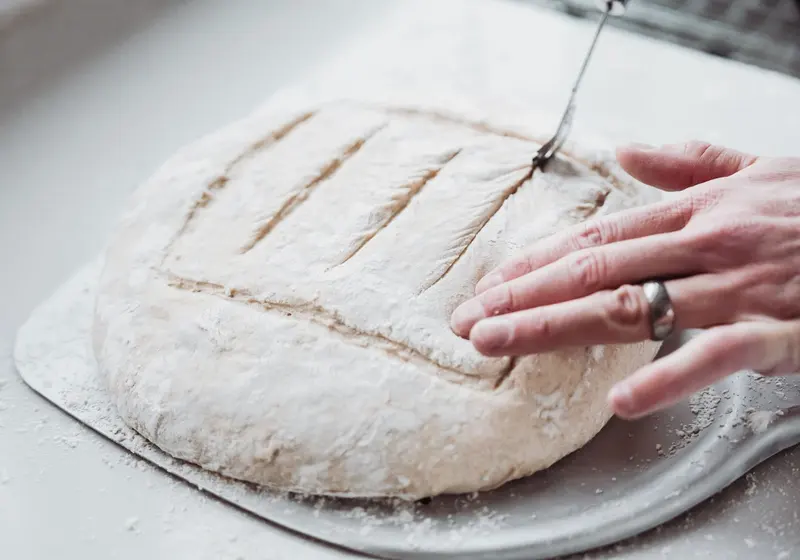 Une main incise la surface d’un pâton fariné avec une lame