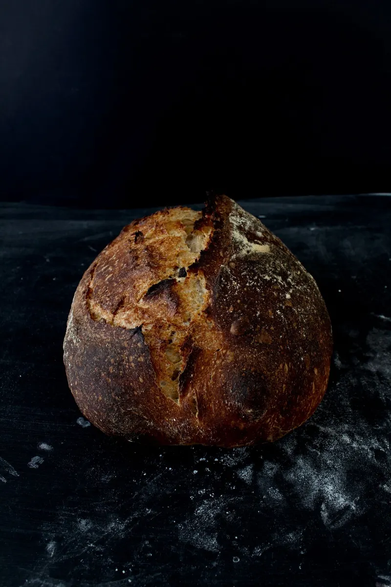 Pain rond à la croûte farinée, posé sur une surface sombre